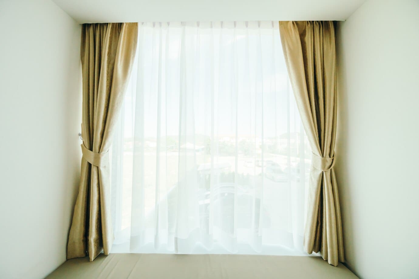 A large window with sheer white curtains and beige drapes, allowing natural light to illuminate the room.