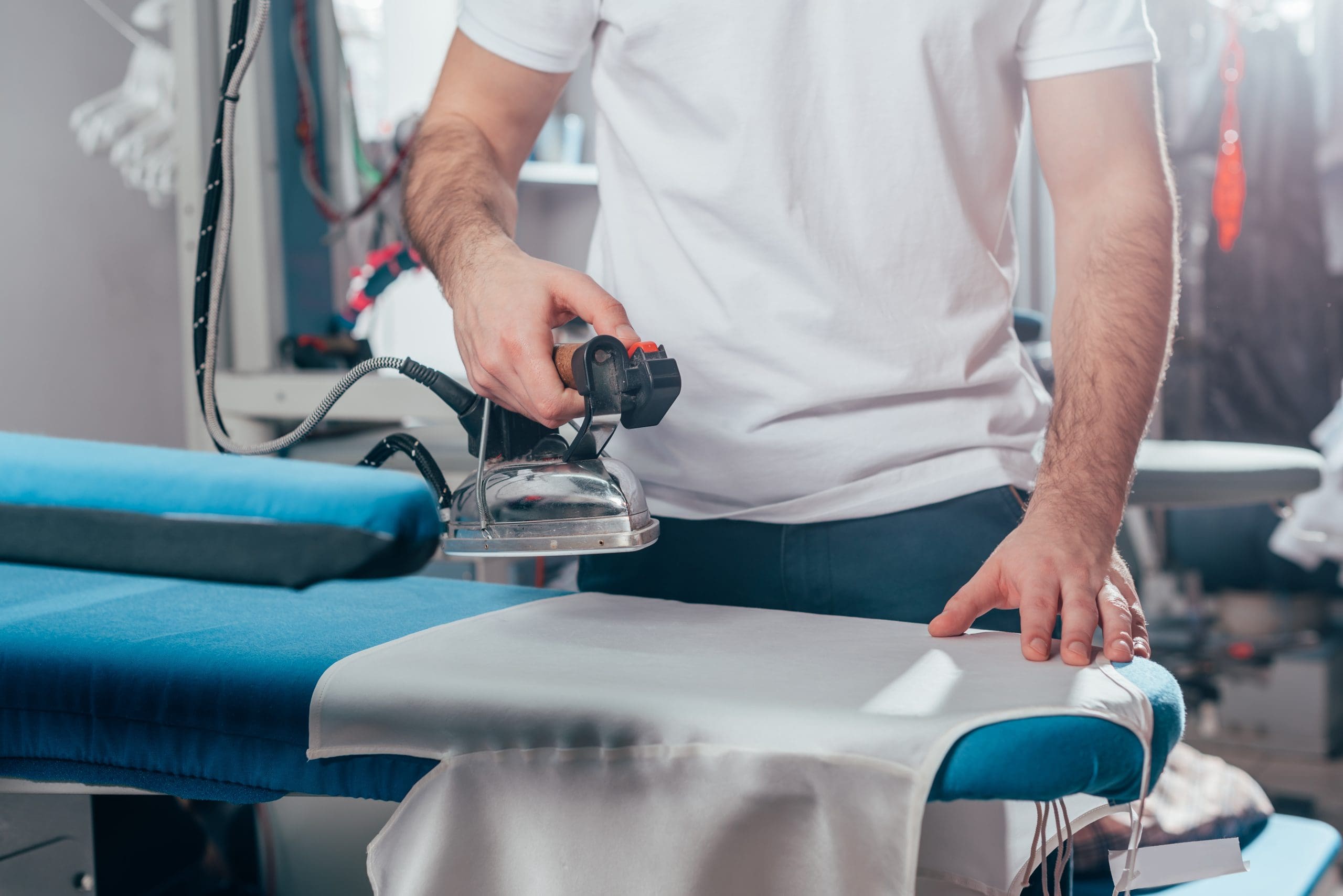 A person skillfully using a handheld steam iron on a piece of fabric atop a blue ironing board, achieving results that rival professional dry cleaning.