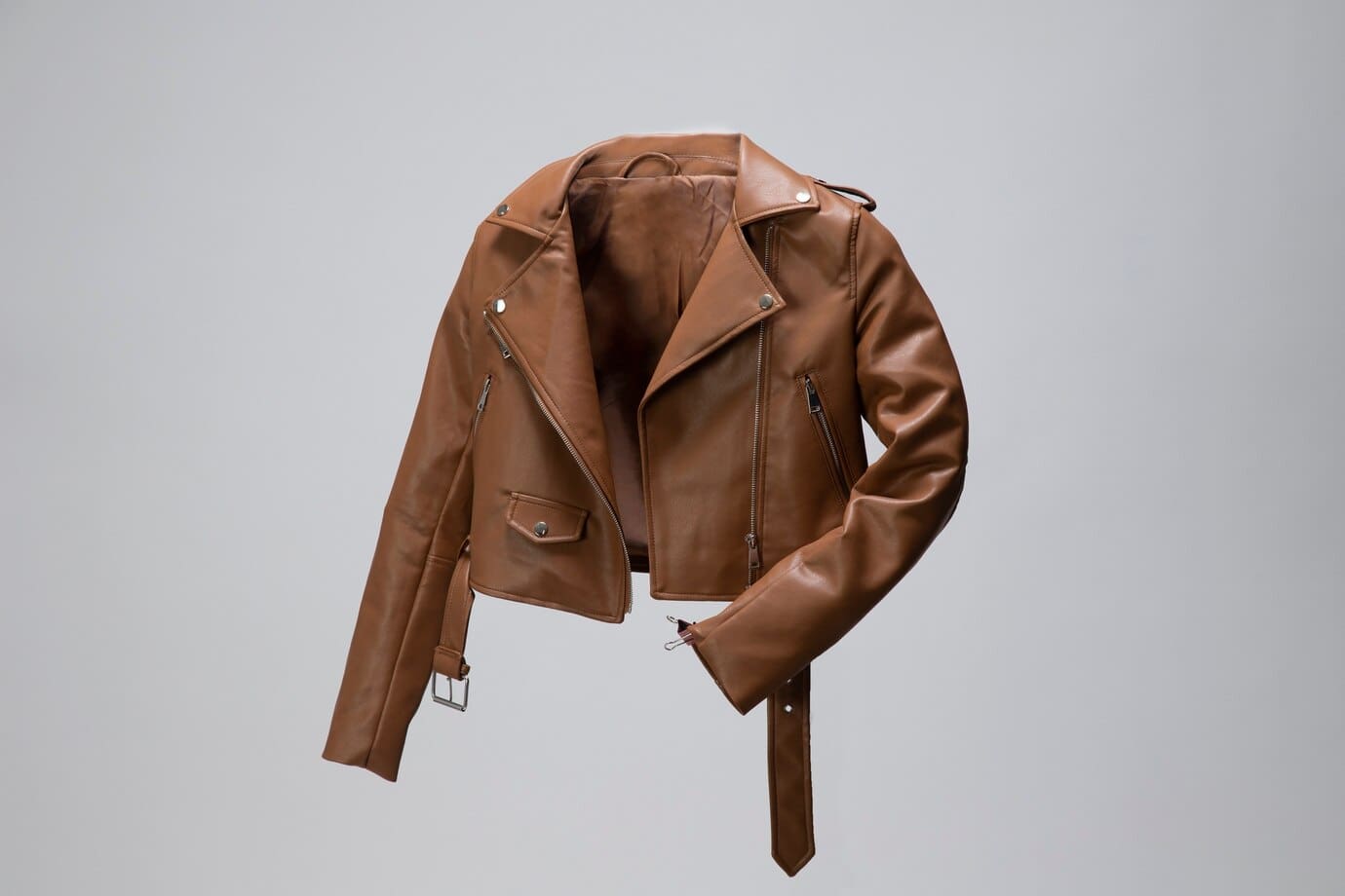 Brown leather jacket with a notched lapel, zippered pockets, and a belted waist, displayed against a plain gray background.