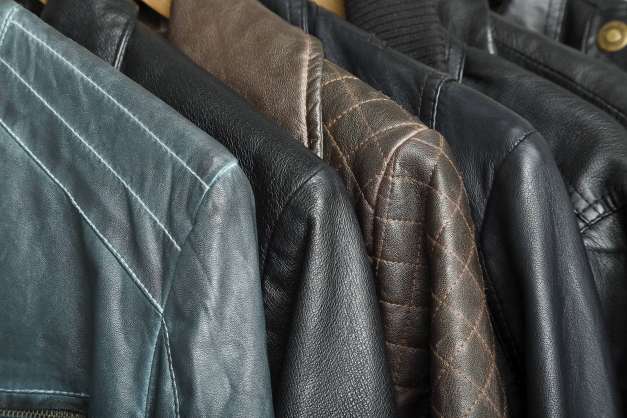 Several leather jackets in different colors and textures hang on wooden hangers in a row.